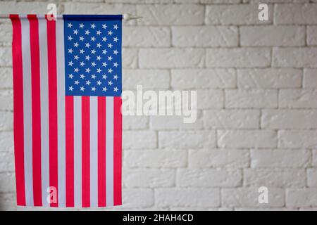 Auf der linken Seite des Rahmens ist die US-Flagge vor dem Hintergrund einer SCHWEREN, VERBLURTEN Ziegelmauer zu sehen. Auf der rechten Seite befindet sich ein leeres Leerzeichen zum Einfügen von Text. Blurre Stockfoto