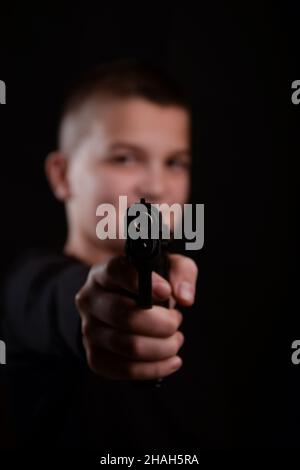 Ein junger Mann zielt auf einen Schuss aus einer Pistole. Die Waffe ist im Fokus, und alles andere und das Gesicht der Person ist verschwommen und unscharf. Studio sh Stockfoto