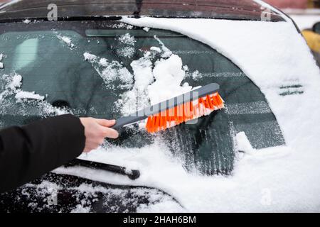 Winterprobleme mit dem Auto. Ein Mann reinigt das Auto mit einer Bürste vom Schnee Stockfoto