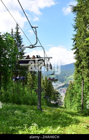 Ein Lift mit vielen Bänken führt die Menschen den baumbedeckten Berg hinunter. Das Foto wurde im Sommer gegen einen blauen Himmel aufgenommen. Stockfoto