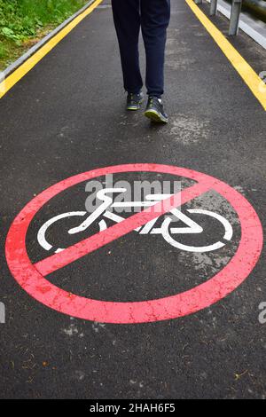 Auf dem asphaltierten Fußgängerweg im Vordergrund befindet sich ein Schild, das nicht für Radfahrer zugelassen ist. Im Hintergrund sind t Stockfoto