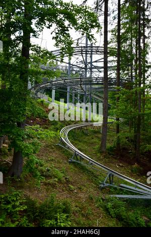 Im Wald am Sommerhang des Berges gibt es eine Achterbahnfahrt leer, ohne Menschen. Die Schienen winden sich zwischen den Bäumen Stockfoto