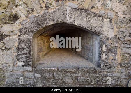 Eine Schießschlange in der dicken Mauer einer alten Festung oder Burg. Bedeckt mit rauem Stein Stockfoto