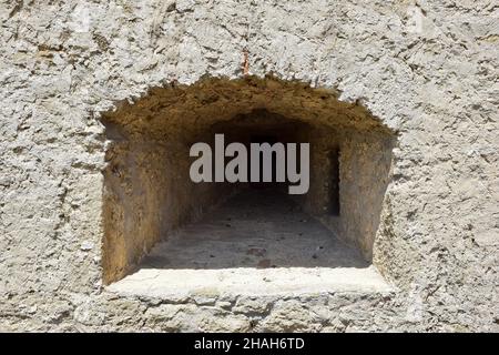 Eine Schießschlange in der dicken Mauer einer alten Festung oder Burg. Bedeckt mit rauem Stein Stockfoto