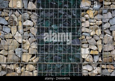 Ein dekorativer Zaun aus Steinen hinter Gittern und gebrochenem großen Glas in der Mitte. Fotografiert im Vollformat Stockfoto