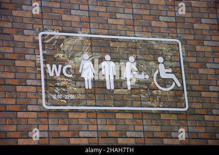 Es gibt ein Schild an der Ziegelwand mit symbolischen verschiedenen Symbolen für die Bezeichnung der Toilette Stockfoto