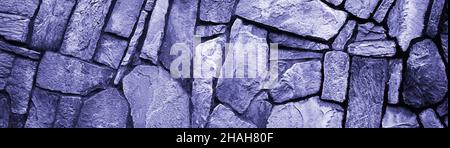 Die Wand Naturstein, das Mauerwerk ist Stein auf Zement. Konzept - Steintapete, Hintergrund und Dekor, Farbe 2022 sehr peri Lavendel. Stockfoto