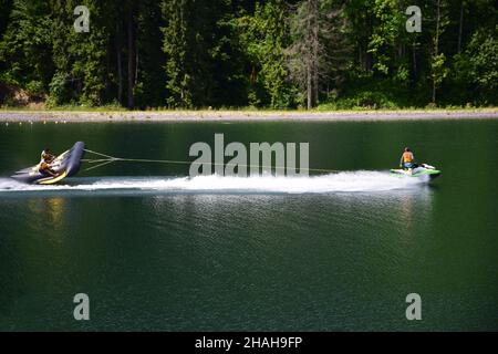 Ein Jet-Ski mit hoher Geschwindigkeit zieht mit zwei Männern ein aufblasbares Sportfloß und unterhält sie Stockfoto