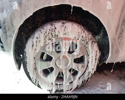 Das Rad des Wagens und ein Teil des Kotflügels des Wagens sind alle vollständig mit weißem Schaum bedeckt, der für das Abwaschen mit Wasser vorbereitet ist. F Stockfoto