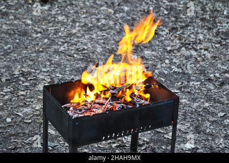 Ein helles Feuer in einem eisernen Feuerholz Holzkohlegrill brennt in einem Waldcamping zum Braten von Fleisch und Gemüse Stockfoto