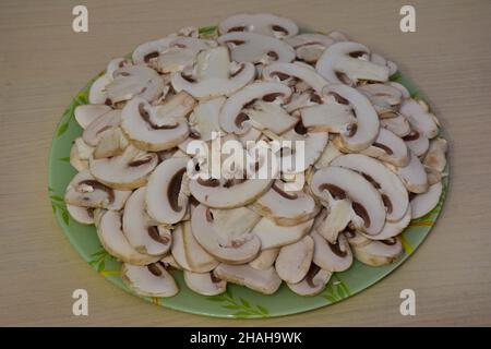 Champignonpilze, die auf einem grünen Glasplatte in der Mitte des Rahmens in Scheiben geschnitten werden, fertig zum Kochen Stockfoto