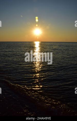 Morgendämmerung Sonne vor dem Hintergrund des Meeres Sandstrand, mit Reflexionen auf den ruhigen Wellen Stockfoto