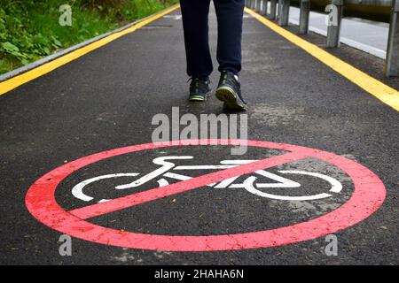 Auf dem asphaltierten Fußgängerweg im Vordergrund befindet sich ein Schild, das nicht für Radfahrer zugelassen ist. Im Hintergrund sind t Stockfoto