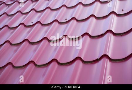 Rotes Welldach in Form von Wellen aus Metallfliesen auf dem gesamten Hintergrund. Stockfoto