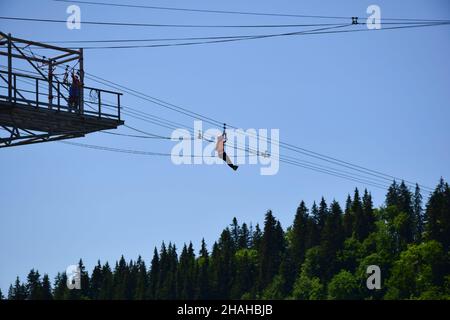 Ein Mädchen von unkenntlich erscheinenden Aussehen steigt vom Turm entlang eines Drahtseiles auf einer Seillinie in großer Höhe herab Stockfoto