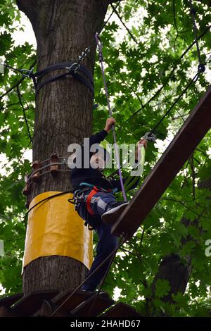 Ein Teenager in einem Schutzhelm klettert in einem Seilpark auf eine Hängeleiter Stockfoto