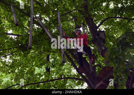 Ein Teenager in einem Sicherheitsgurt überquert eine Hängebrücke in einem Sommerpark Stockfoto