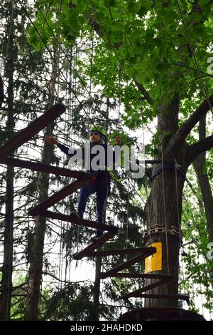 Der junge Teenager klettert in einem Seilpark eine hängende Treppe von einem Baum zum anderen Stockfoto