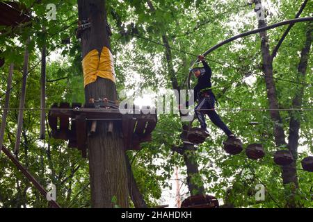 Der junge Teenager klettert in einem Seilpark eine hängende Treppe von einem Baum zum anderen Stockfoto