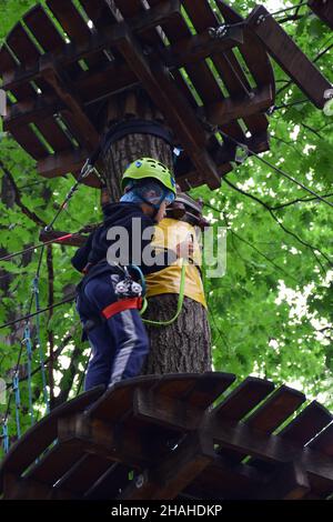 Der junge Teenager klettert in einem Seilpark eine hängende Treppe von einem Baum zum anderen Stockfoto