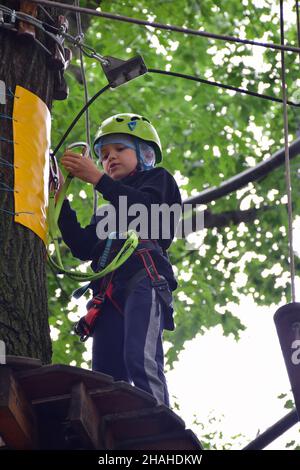 Der junge Teenager klettert in einem Seilpark eine hängende Treppe von einem Baum zum anderen Stockfoto