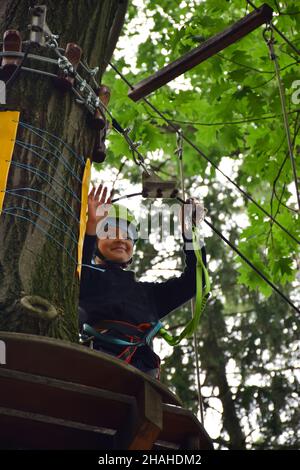 Der junge Teenager klettert in einem Seilpark eine hängende Treppe von einem Baum zum anderen Stockfoto