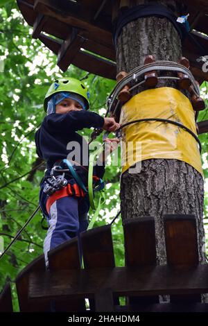 Der junge Teenager klettert in einem Seilpark eine hängende Treppe von einem Baum zum anderen Stockfoto