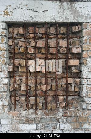 Ein zugemauertes Fenster, das mit einem Gitter in Form einer rostigen Eisenverstärkung geschlossen wird. Mauerwerk achtlos getan Stockfoto