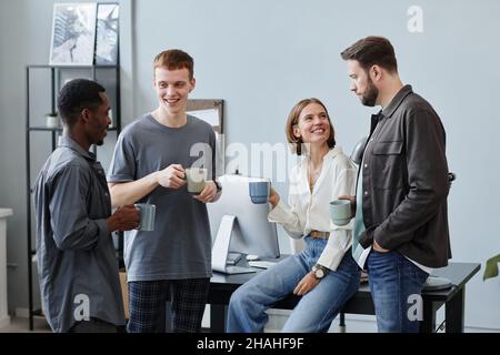 Gruppe von Geschäftsleuten, die Kaffee aus Tassen trinken und während der Kaffeepause im Büro miteinander sprechen Stockfoto