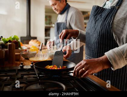 Fröhliches multikulturelles älteres Paar, das in einer modernen Küche gemeinsam gesundes Frühstück kocht. Stockfoto