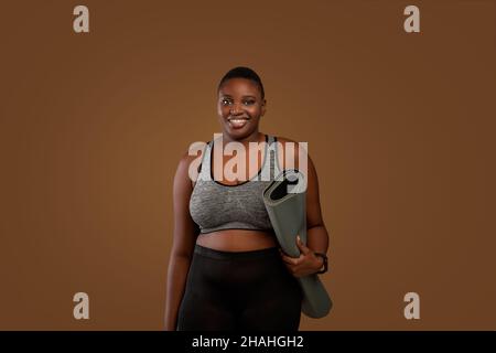 Mollige schwarze Frau mit Yogamatte im Studio Stockfoto
