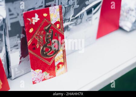 Aufrechter roter Umschlag oder rotes Paket namens Ang Pao oder Ang Pow, auch Hongbao oder Hungbao auf Mandarin und Lai auf Kantonesisch auf weißem Tisch. Stockfoto