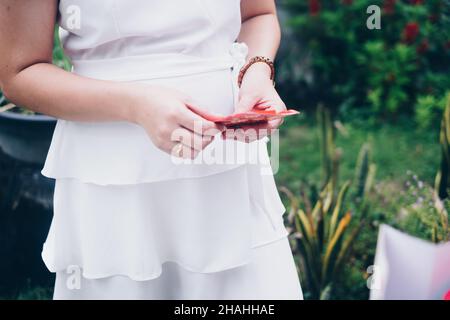 Die Hand einer Frau hält einen geöffneten roten Umschlag oder ein rotes Paket namens Ang Pao oder Ang Pow, ebenfalls Hongbao oder Hungbao auf Mandarin und Lai See auf Kantonesisch. Stockfoto