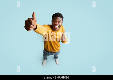 Fröhlicher afroamerikanischer Kerl, der Daumen nach oben zeigt, Draufsicht Stockfoto