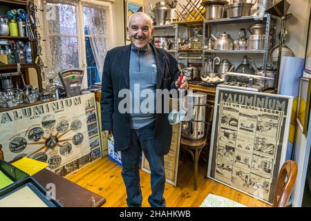 Kader Zennaf lacht und schaut zur Seite, eine Aluminiumschöpfkelle mit rotem Griff in der Hand, vor den überfüllten Regalen seiner privaten Sammlung in Saint-Chamond, Département Loire, Frankreich. Er begann als Kind zu sammeln, nachdem er selbst eine kleine Kaffeetasse aus dem französischen Leichtmetall geschenkt bekommen hatte. Stockfoto