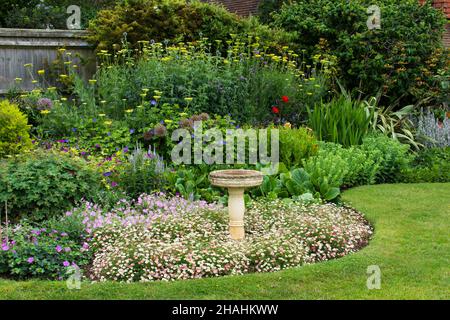 Blick auf eine englische krautige mehrjährige Gartengrenze im Sommer mit Vogelbad als zentraler Schwerpunkt. Stockfoto