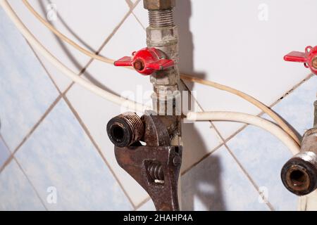 Abschrauben von Armaturen auf Wasserleitung mit altem verstellbaren Schraubenschlüssel. Installation des Wasserhahns auf dem Wasserrohr. Beseitigung von Wasserlecks. R Stockfoto