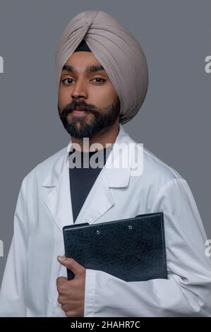 Heiterer Arzt im Turban, der für die Kamera posiert Stockfoto