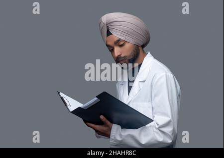 Gutaussehender fokussierter männlicher Arzt, der seine Patientenakten untersucht Stockfoto