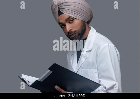 Ruhiger indischer Arzt im Turban, der medizinische Dokumente hält Stockfoto