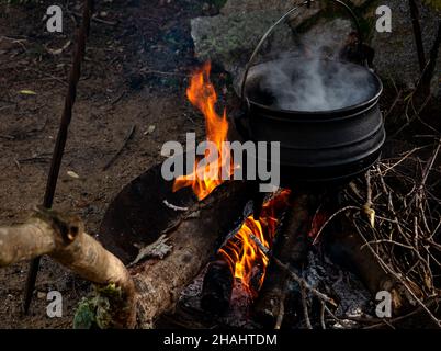 Mittelalterliche Nachstellung, Lagerküche mit Kessel, offenes dampfendes heißes Metall auf Feuer, während heiße Suppe gekocht wird. Mittelalterliche Küchenutensilien Stockfoto