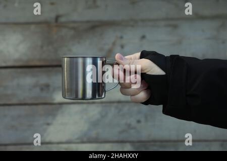 Männliche Hand hält Metallbecher auf Holzhintergrund Stockfoto