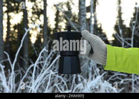 Hand in Fäustling hält die Kaffeemaschine im Wald Stockfoto