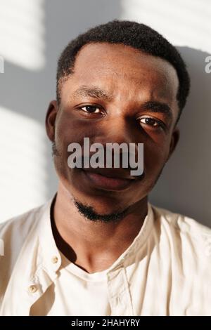 Nahaufnahme eines afrikanischen jungen Mannes im Hemd, der isoliert auf weißem Hintergrund auf die Kamera blickt Stockfoto