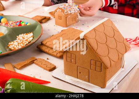 Kinder bauen und dekorieren ein Lebkuchenhaus zur Weihnachtszeit. Weihnachten Familientradition, Weihnachtshandwerk. Stockfoto