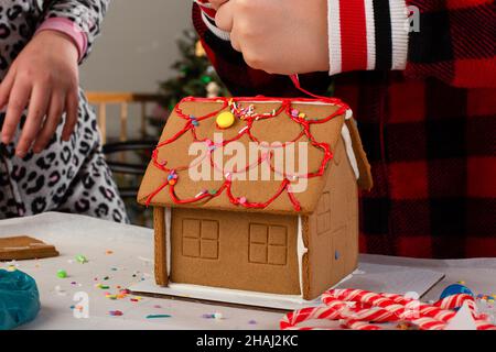 Kinder bauen und dekorieren ein Lebkuchenhaus zur Weihnachtszeit. Weihnachten Familientradition, Weihnachtshandwerk. Stockfoto