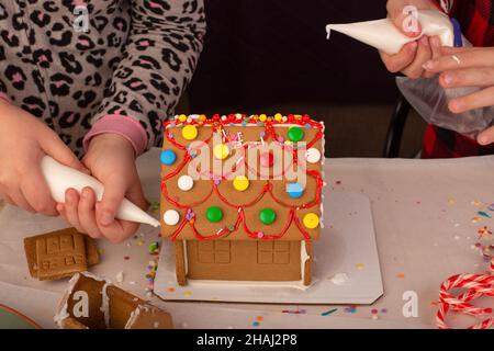 Kinder bauen und dekorieren ein Lebkuchenhaus zur Weihnachtszeit. Weihnachten Familientradition, Weihnachtshandwerk. Stockfoto