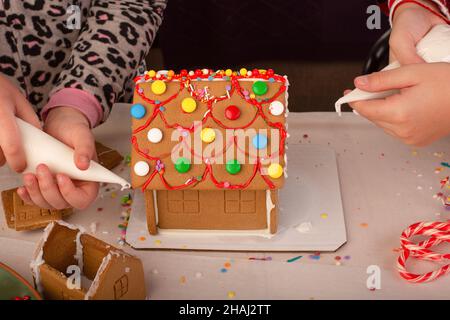 Kinder bauen und dekorieren ein Lebkuchenhaus zur Weihnachtszeit. Weihnachten Familientradition, Weihnachtshandwerk. Stockfoto