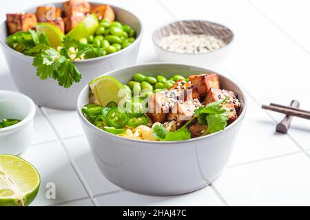 Vegane Nudeln Ramen Suppe mit marinierten Tofu, edamame Bohnen und Paprika in einer grauen Schüssel auf weißem Fliesengrund. Stockfoto