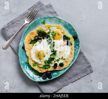 Türkische Eier Fladenbrot mit Joghurt, Käse, Oliven, Spinat und rotem Pfeffer auf Keramik-Vintage-Teller auf grauem altem Hintergrund. Draufsicht. Stockfoto